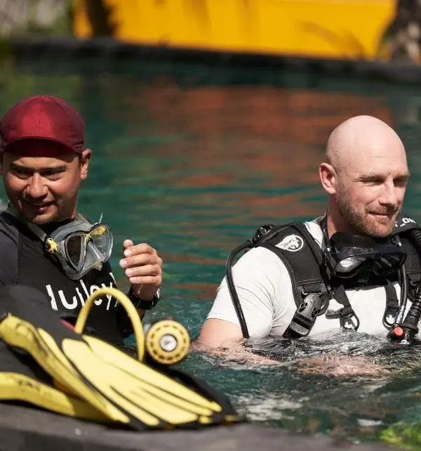 Dos buceadores en el agua preparándose para inmersión en Nusa Penida, con equipo de snorkel y aletas amarillas en primer plano.