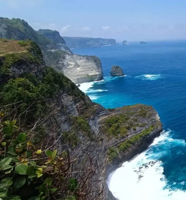 Acantilados de Nusa Penida con olas rompiendo en la base y agua turquesa, vista panorámica del litoral y formaciones rocosas.